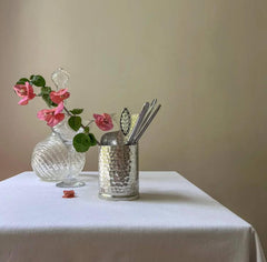 Handmade decorative utensil holder filled with cutlery next to glass vase and flowers