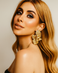 Model wearing large gold statement earrings with artistic texture