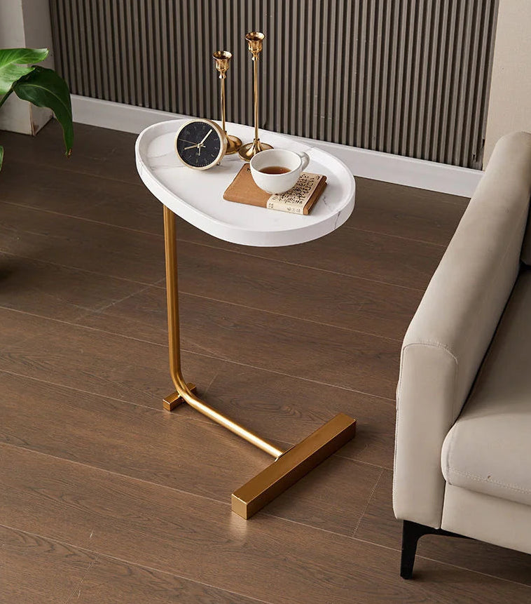 Small round white table with gold legs next to a beige sofa on a wooden floor.