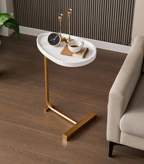 Small round white table with gold legs next to a beige sofa on a wooden floor.
