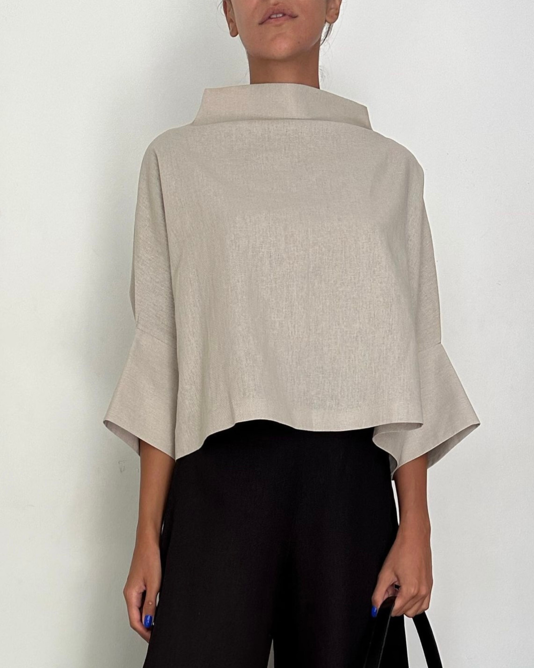 Beige linen boxy blouse with funnel neck and wide sleeves on light background