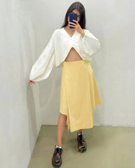 Person wearing a white blouse with cut-out design and a yellow skirt, standing against a plain background.