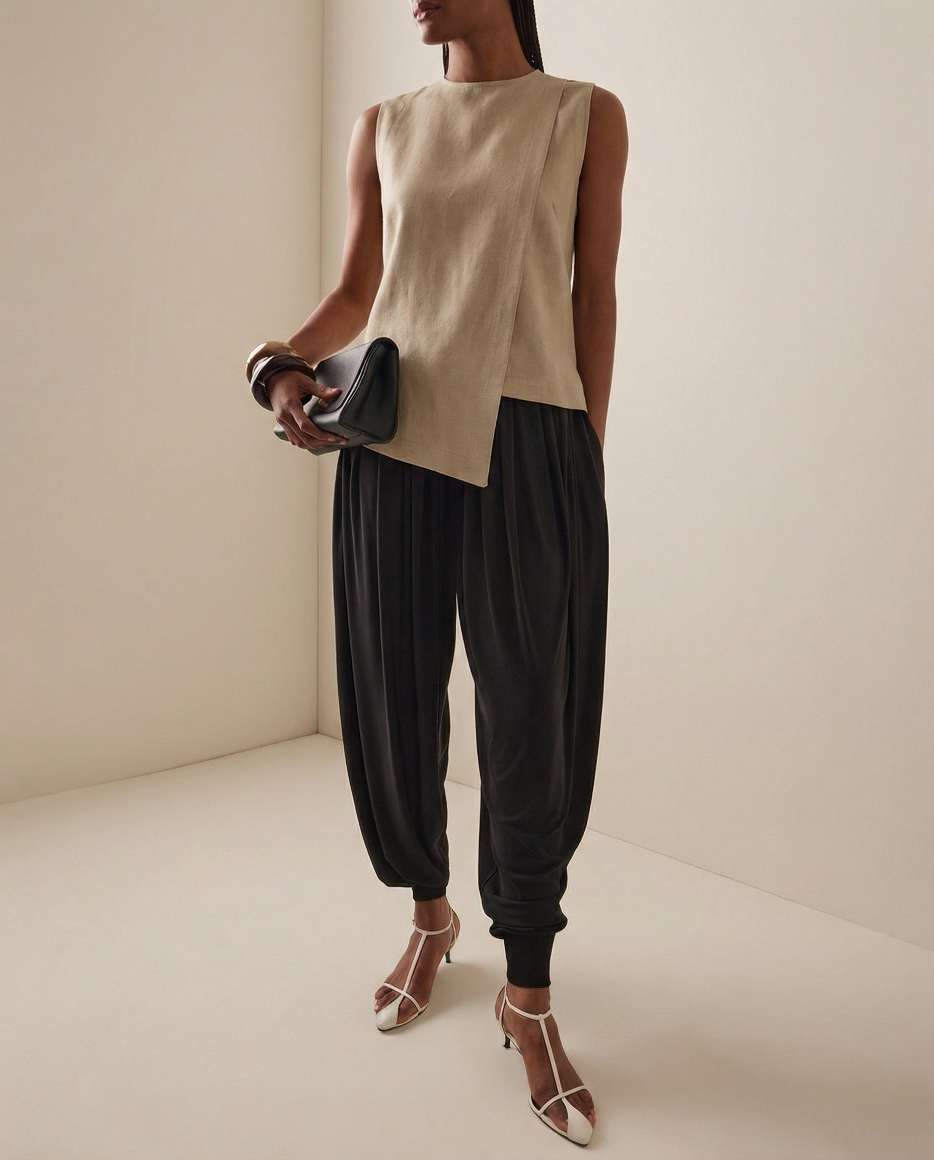 Woman wearing a statement linen beige sleeveless top and black high-waisted pants, holding a clutch.