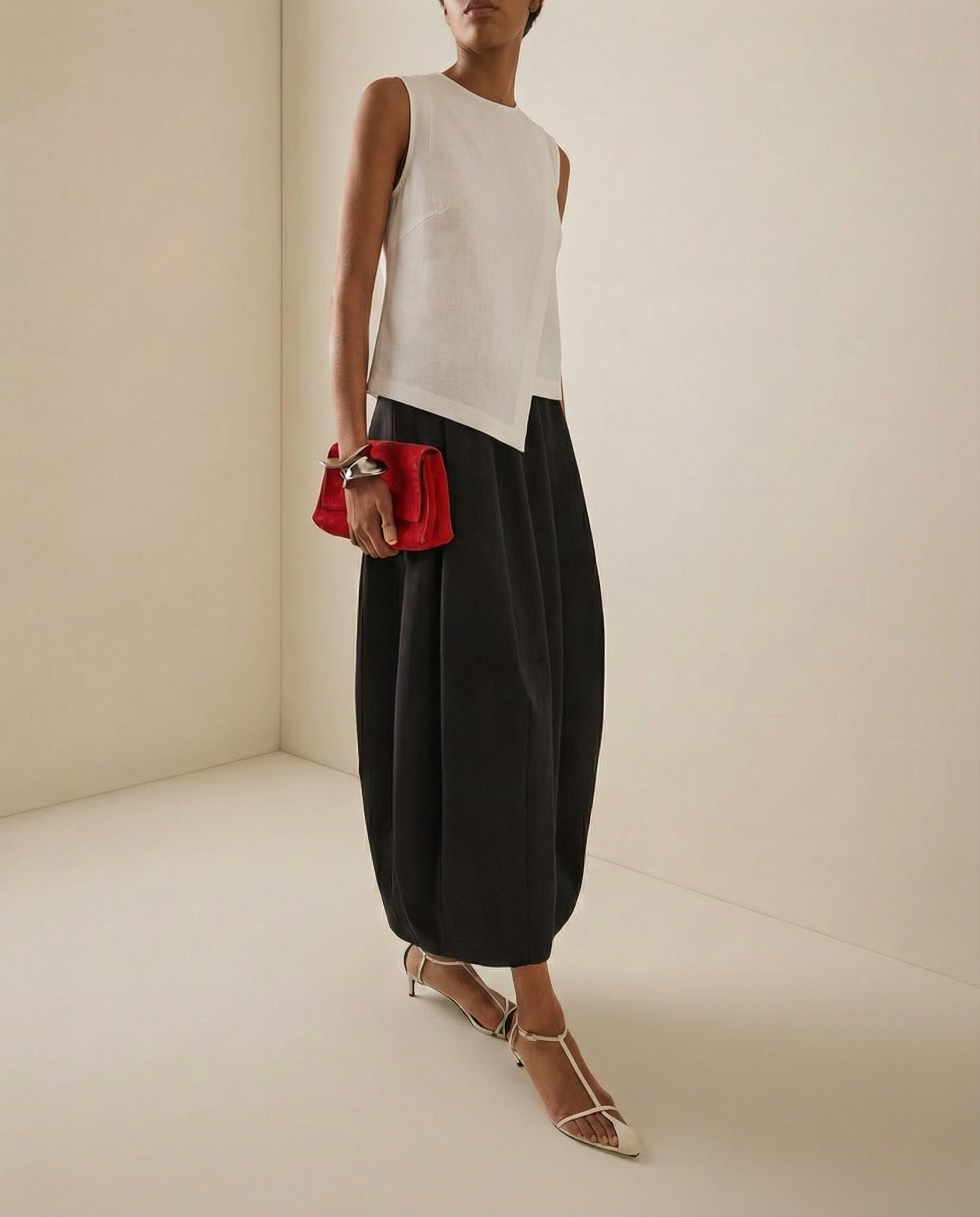 Person wearing a white linen sleeveless top and black high-waisted pants, holding a red clutch.