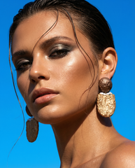 Woman wearing large, ornate earrings against a clear blue sky