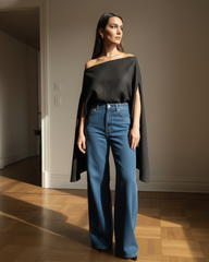 Woman wearing a black off-shoulder top and blue jeans standing in a room with wooden flooring.