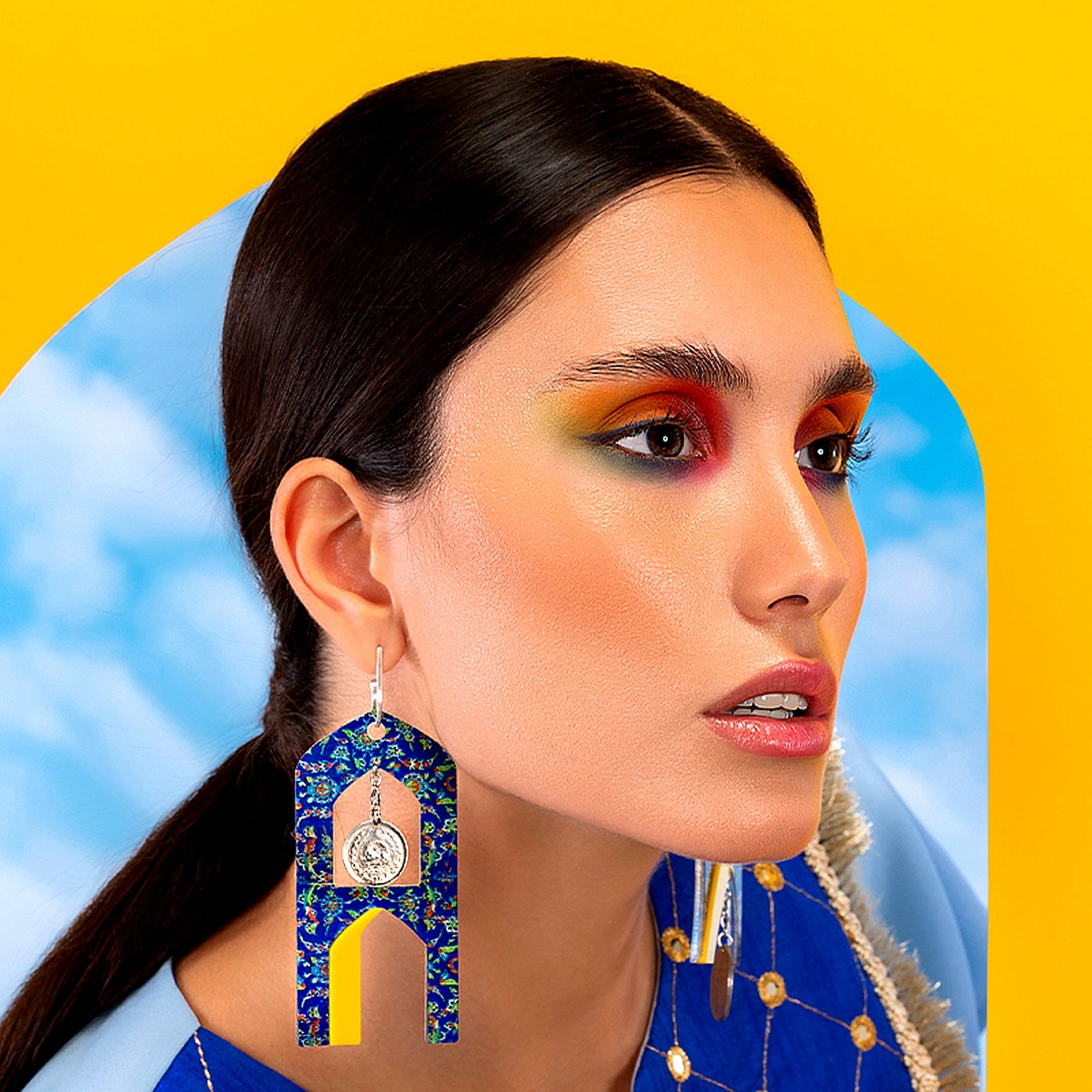 Model wearing handmade coin drop earrings with traditional motif and bold yellow and blue color palette