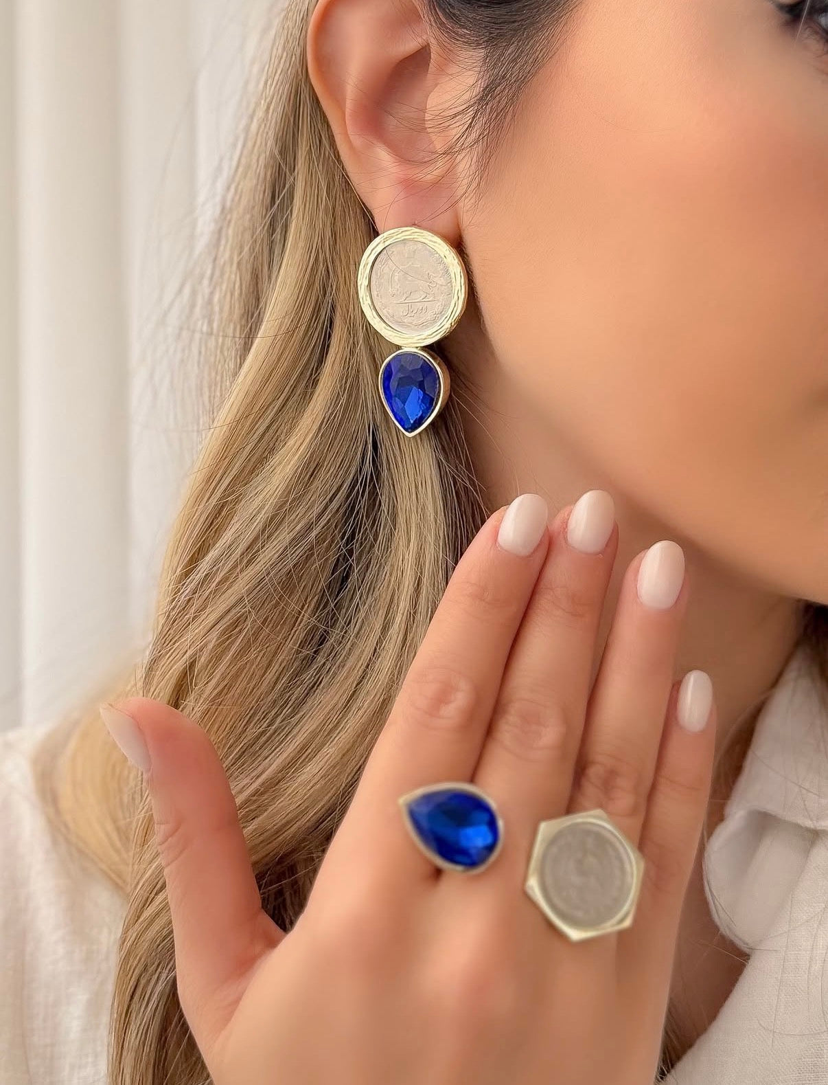 Close-up of a person wearing gold and blue gemstone earrings and rings.