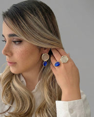 Woman wearing gold and blue earrings with a neutral background