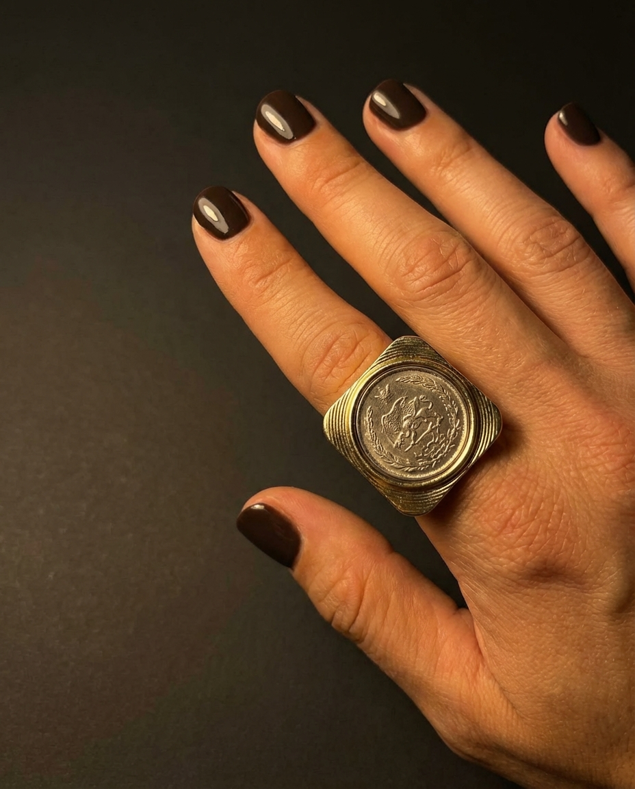 Hand wearing a large coin ring on a dark background