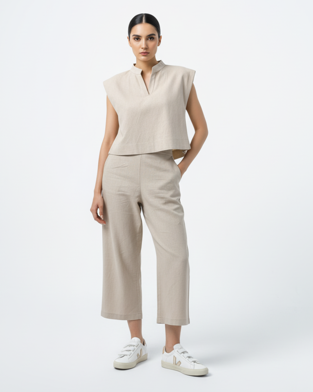 Model wearing a beige linen two-piece set with cap sleeves and cropped wide-leg trousers, styled with white Veja sneakers.