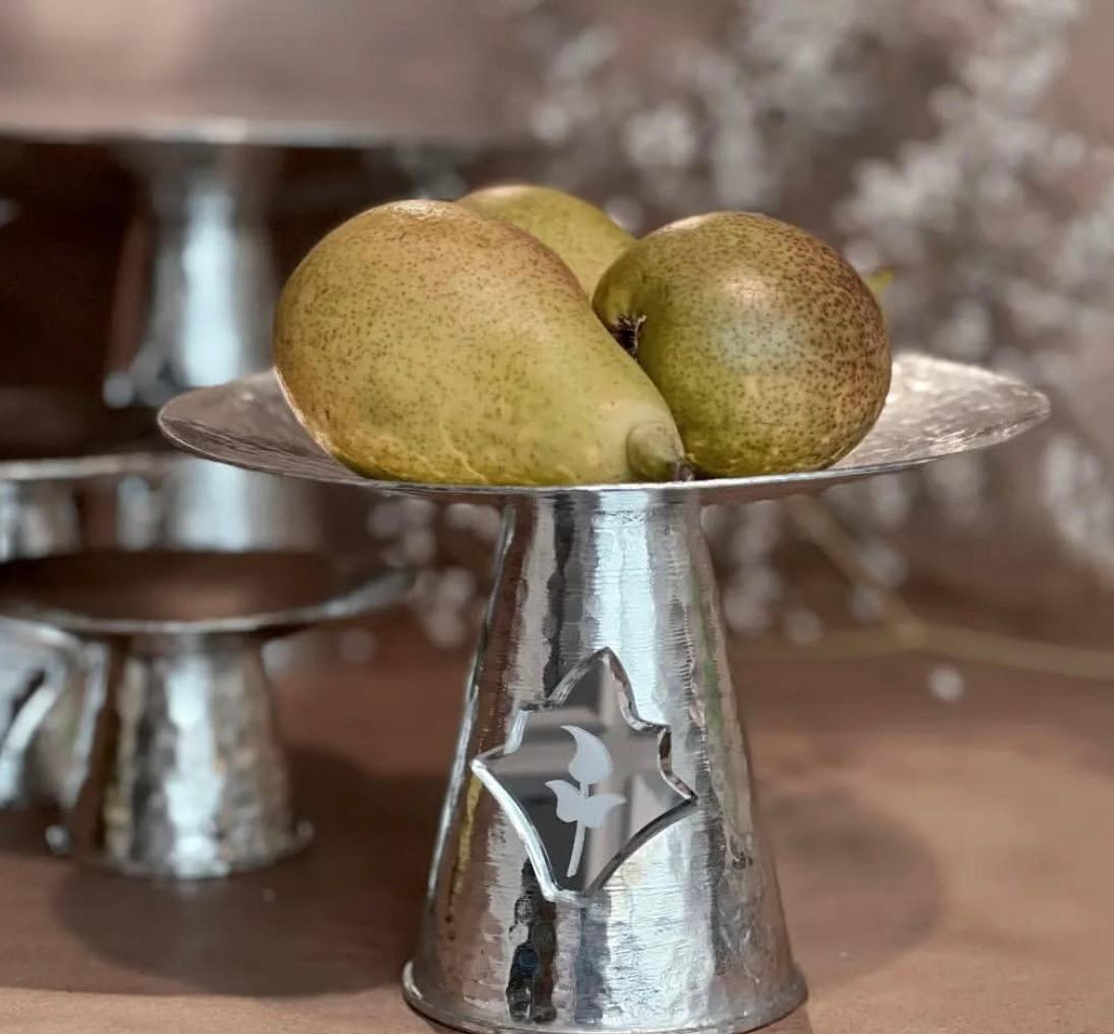 Close-up of hammered copper stand with mirror inlay and pears placed on top