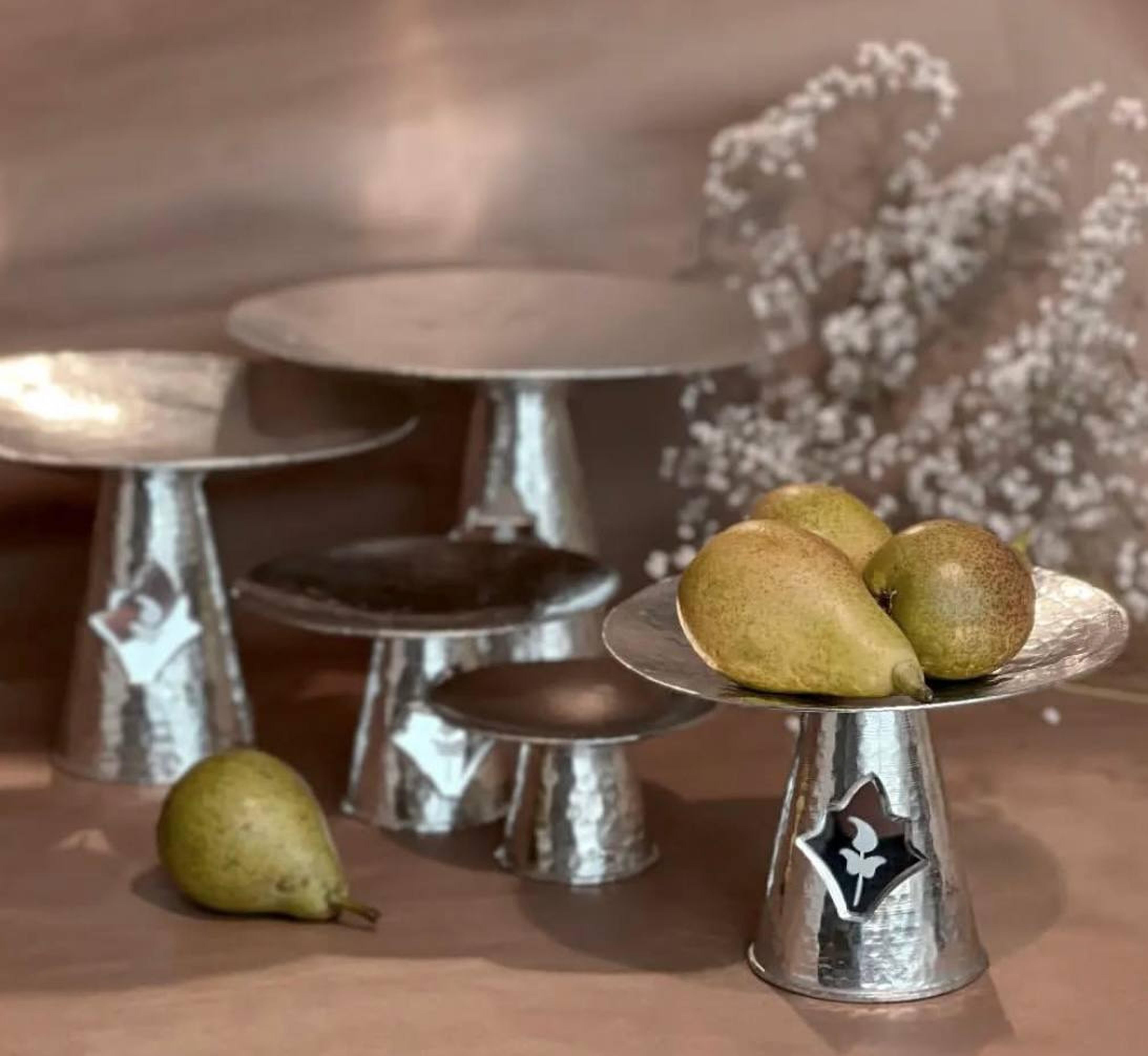 Handmade copper pedestal with mirror floral cut-out used as a fruit stand on table