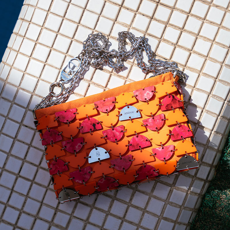 Orange handbag with pink heart patterns and a silver chain on a tiled surface