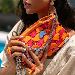Woman holding a colorful handbag with heart patterns and chain details.