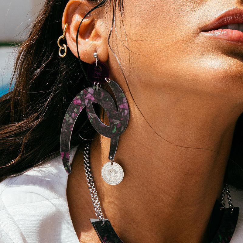 Close-up of a person wearing floral hoop earrings with a coin charm.
